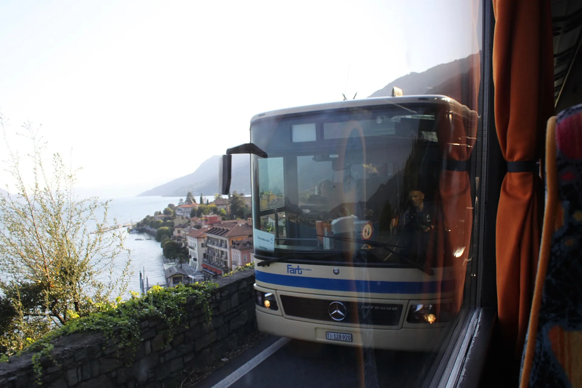 Un autobus di linea sulla strada costiera del Lago Maggiore, con un borgo sullo sfondo
